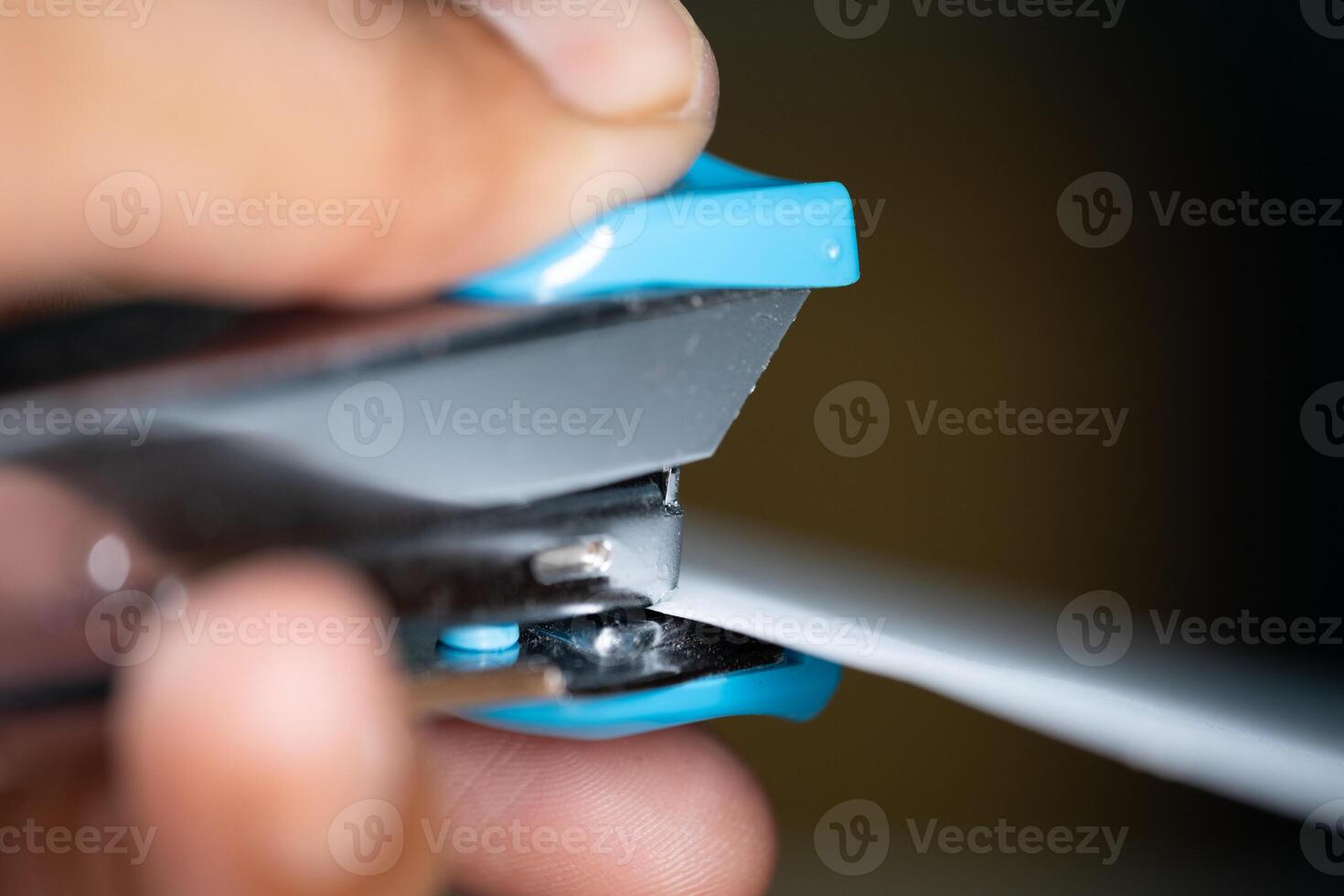 Hand using blue stapler to staple paper photo