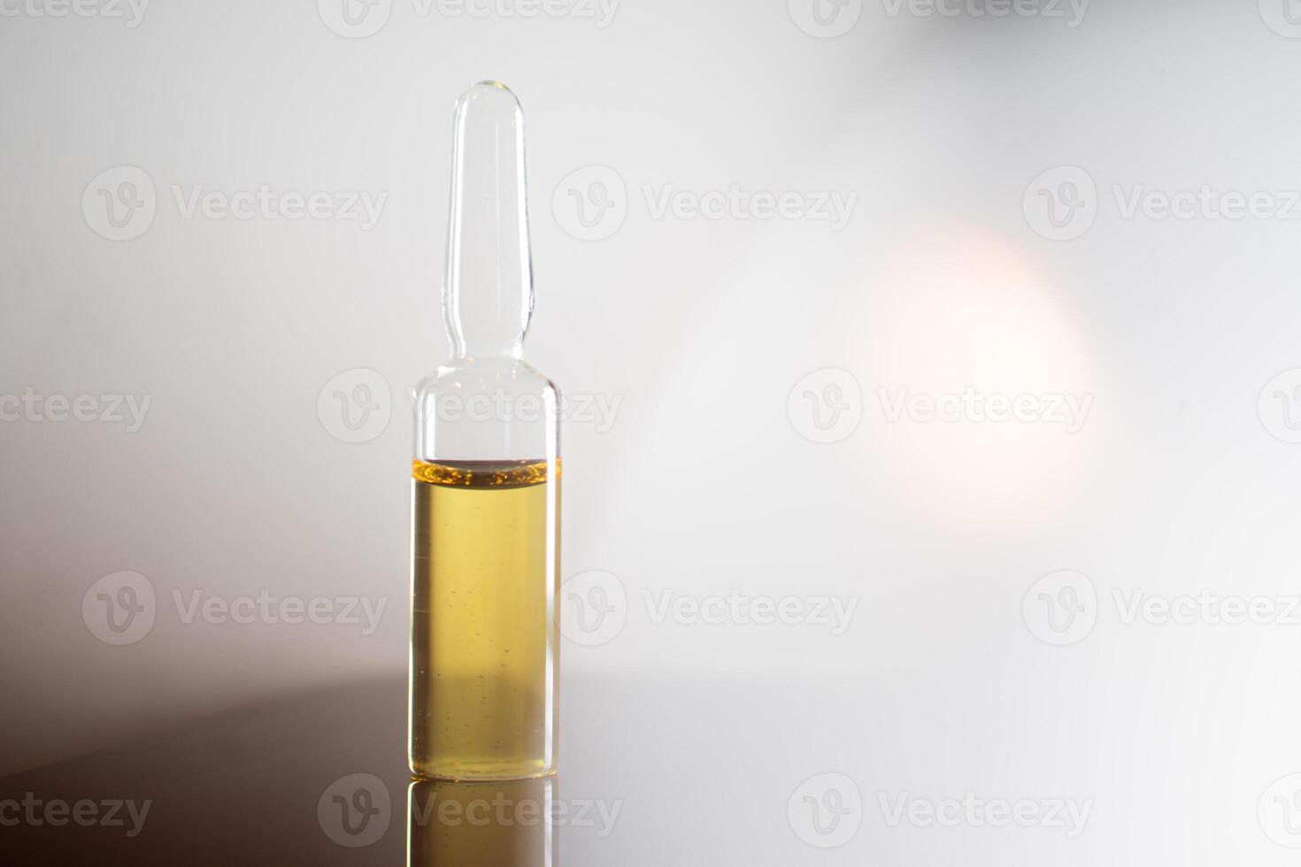Glass ampoule with yellow liquid on reflective surface photo
