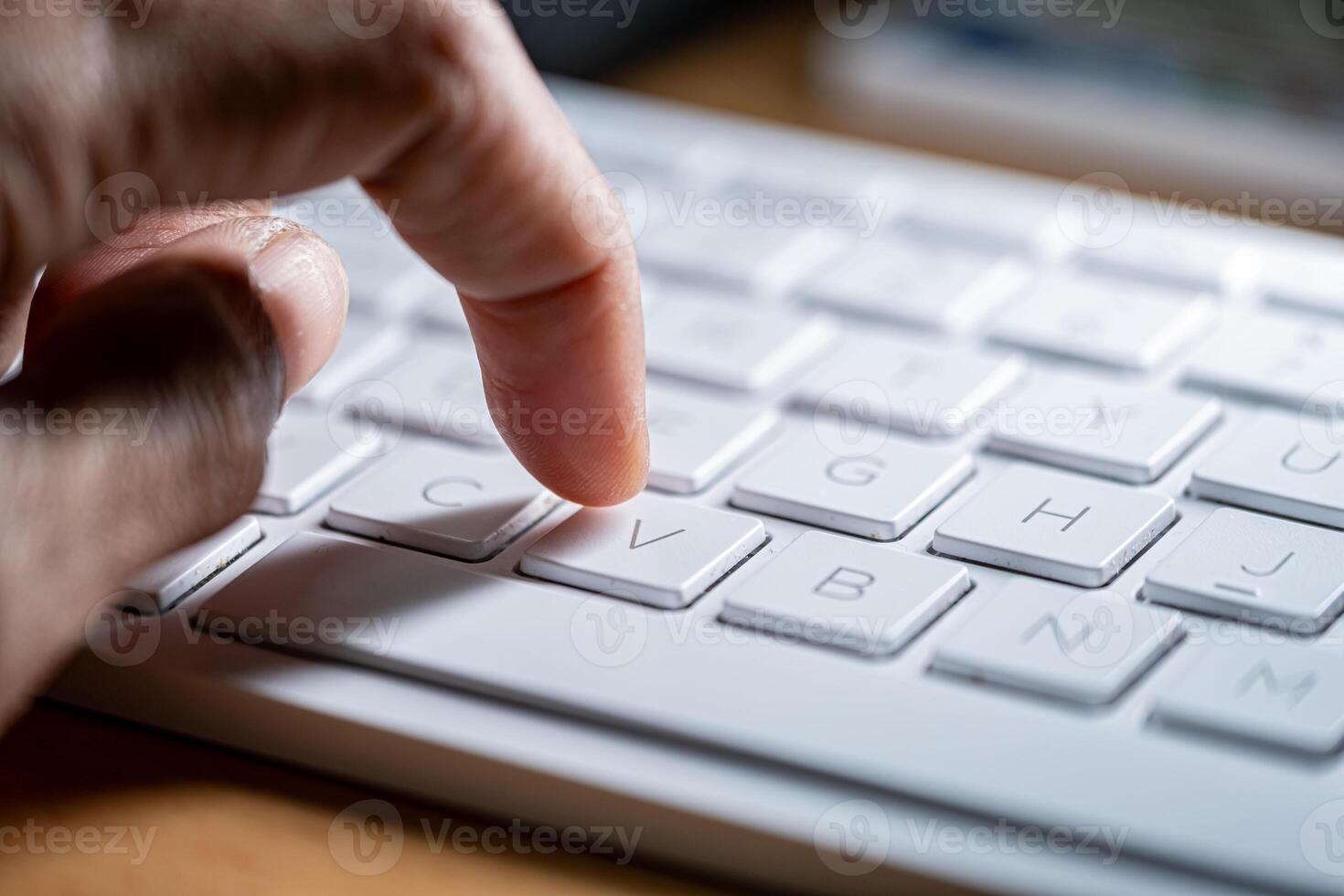 Finger pressing 'V' key on white keyboard photo