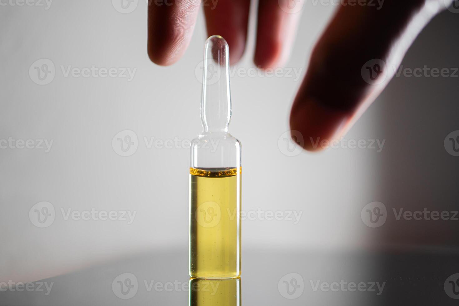 Hand reaching for glass vial with yellow liquid photo