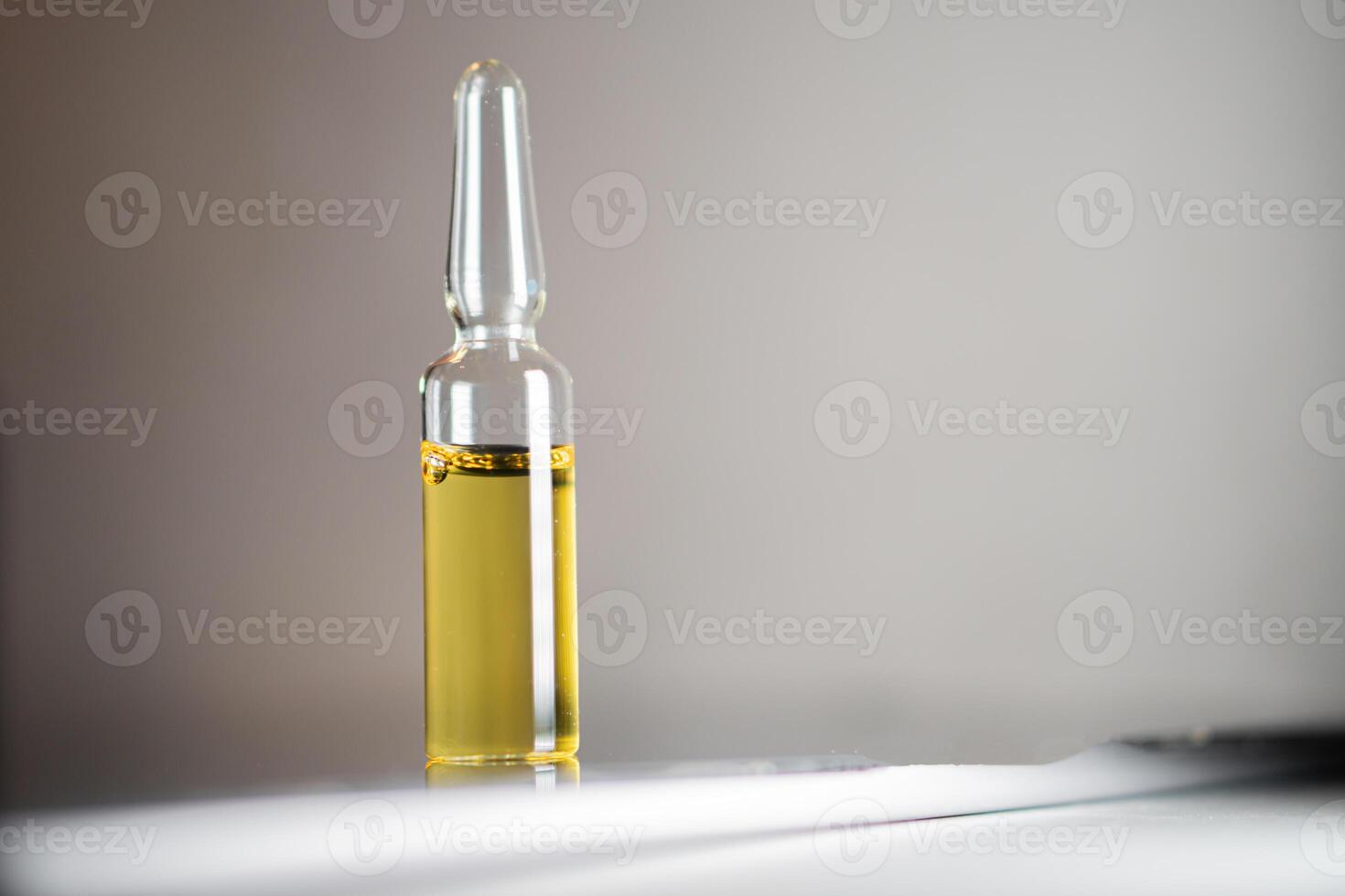 Glass ampoule with yellow liquid on reflective surface photo