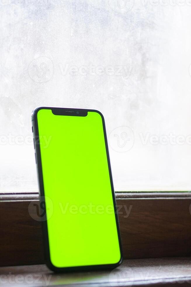 Smart phone with green screen by window photo