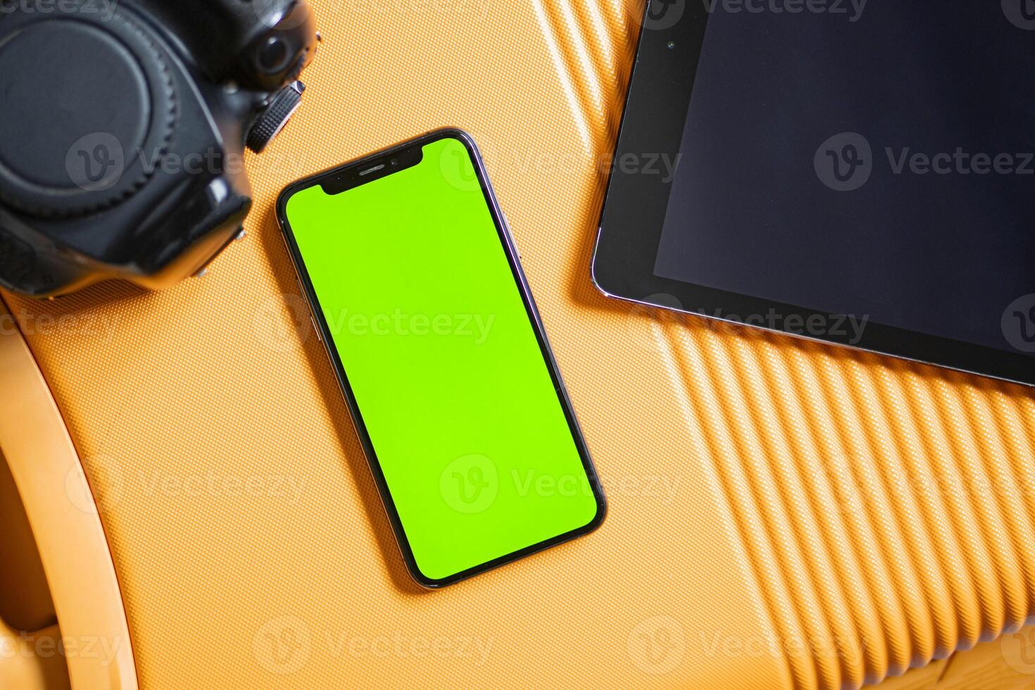Smart phone with green screen and tablet on orange surface photo