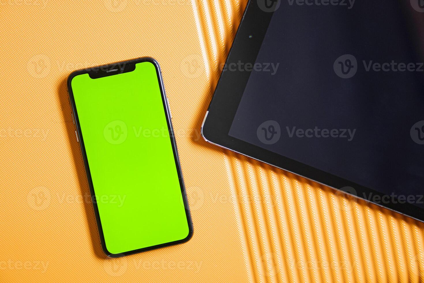 Smart phone with green screen and tablet on orange surface photo
