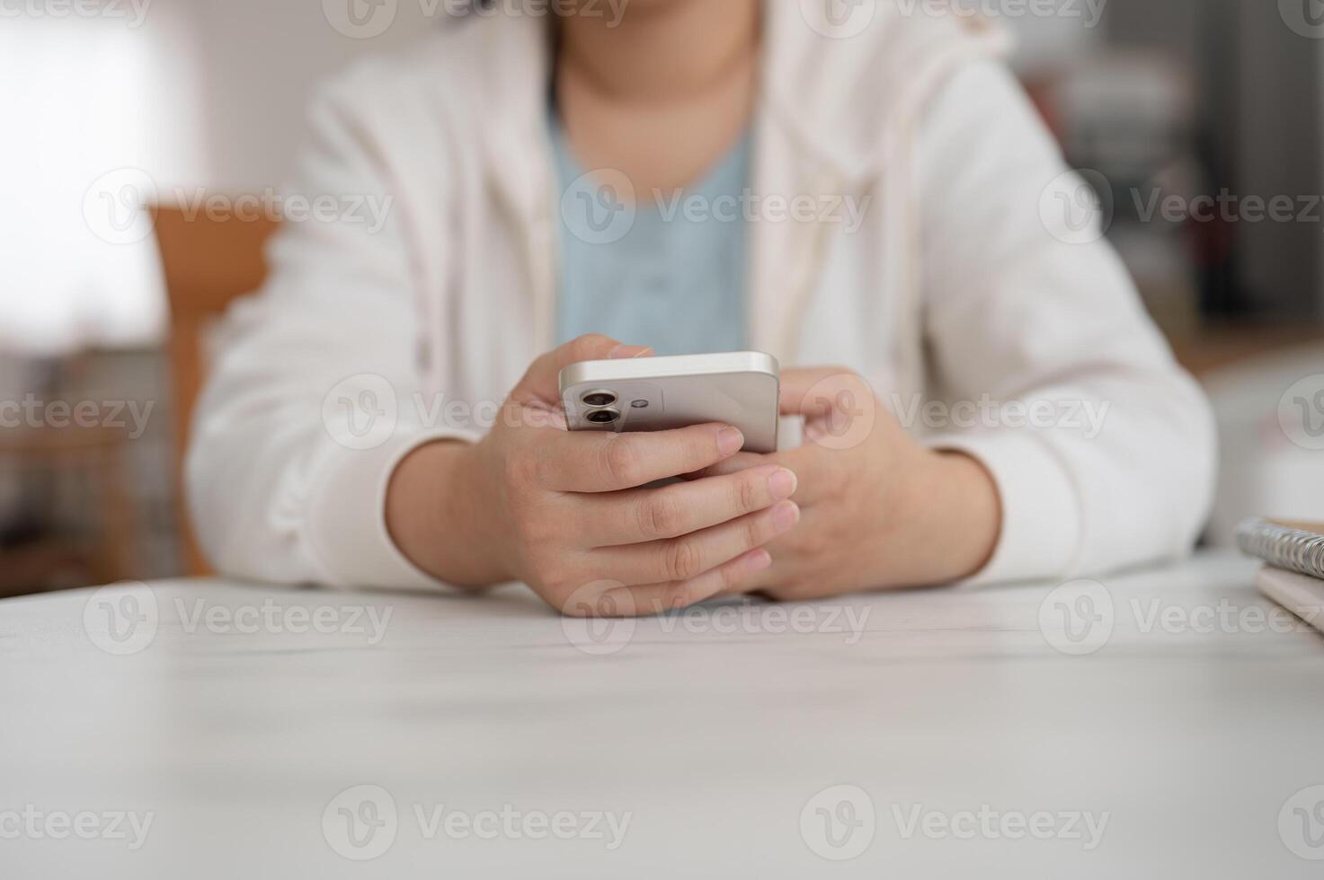 Cropped image of a woman in a hoodie sits in a cafe and uses her smartphone, scrolling on her phone. photo