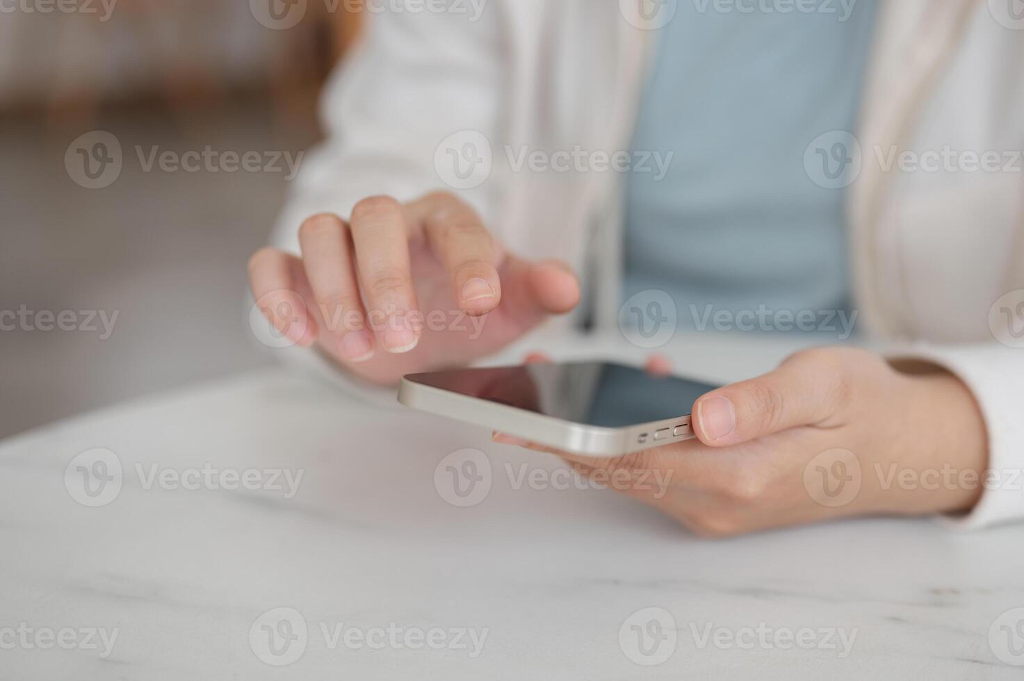 Cropped image of a woman in a hoodie sits in a cafe and uses her smartphone, scrolling on her phone. photo