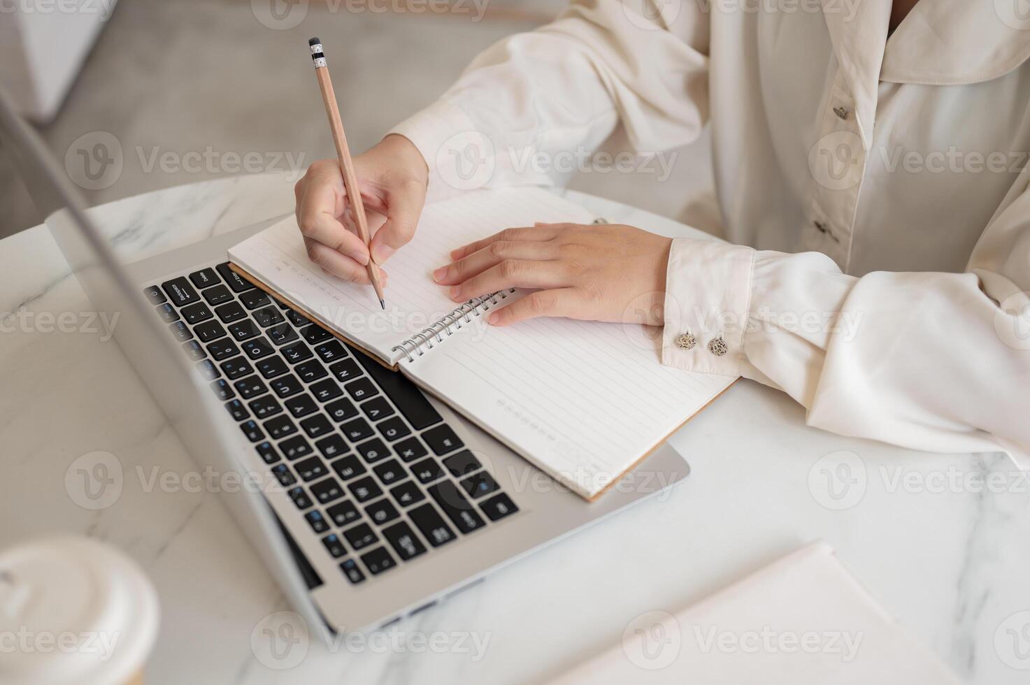 A close-up image of a woman writing something in her notebook and working on her laptop in a cafe. photo