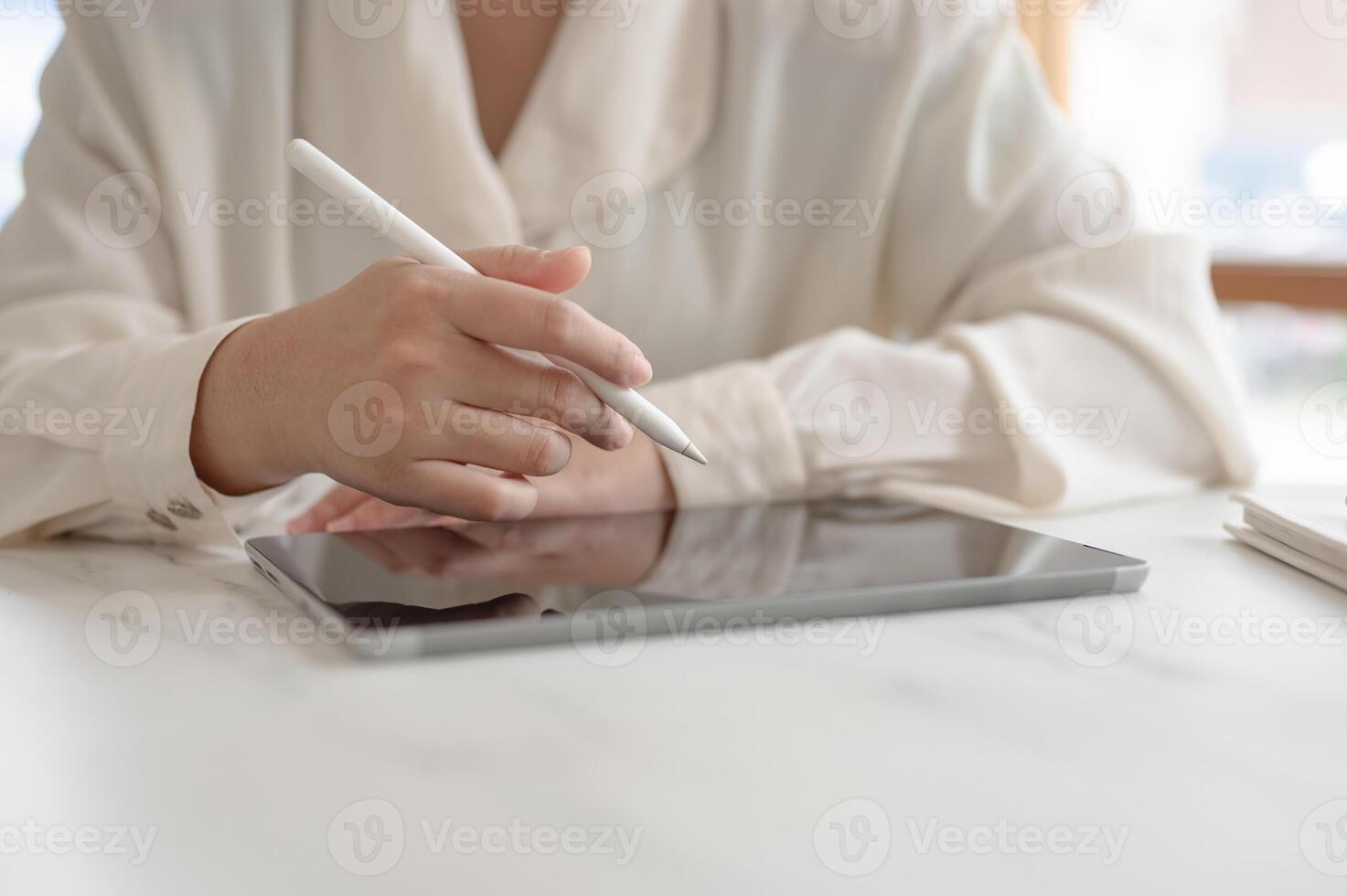 A woman working remotely from a cafe, holding a stylus pen and working on her digital tablet. photo