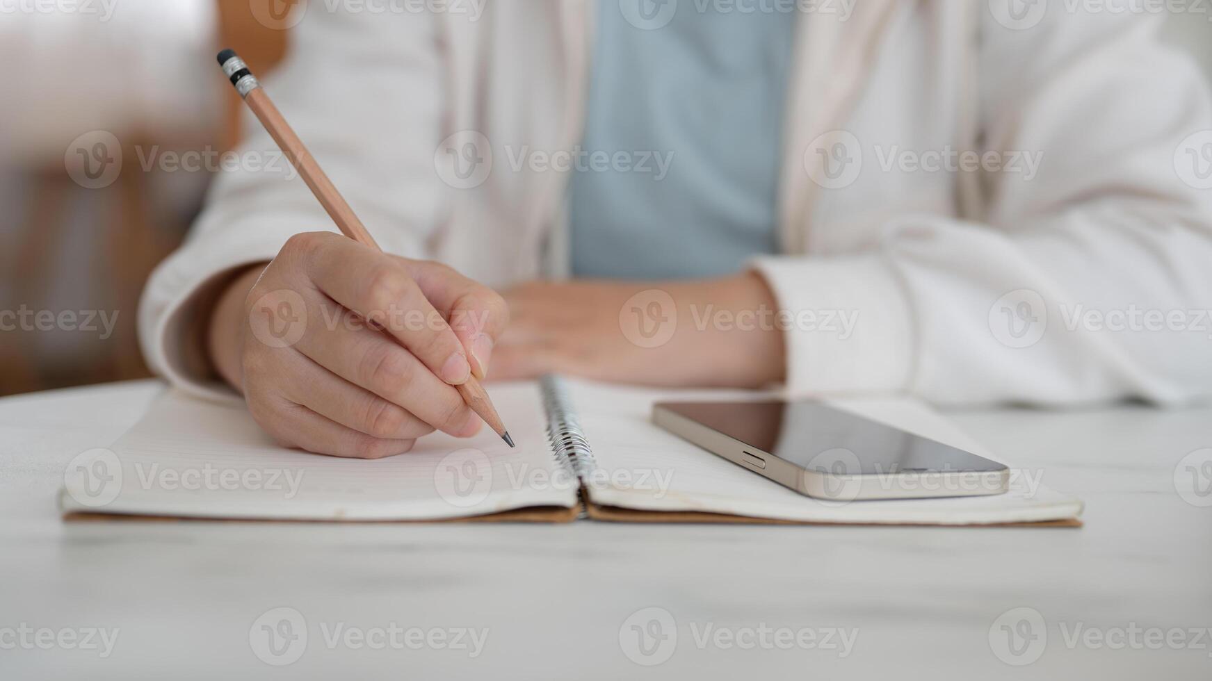 A close-up image of a woman sits in a cafe, writing something in her notebook with a pencil. photo