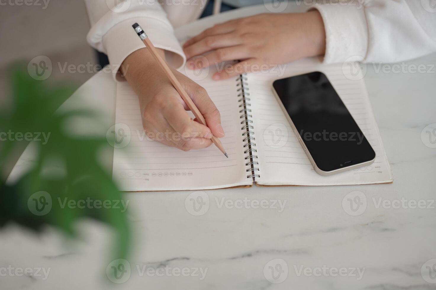 A close-up image of a woman sits in a cafe, writing something in her notebook with a pencil. photo