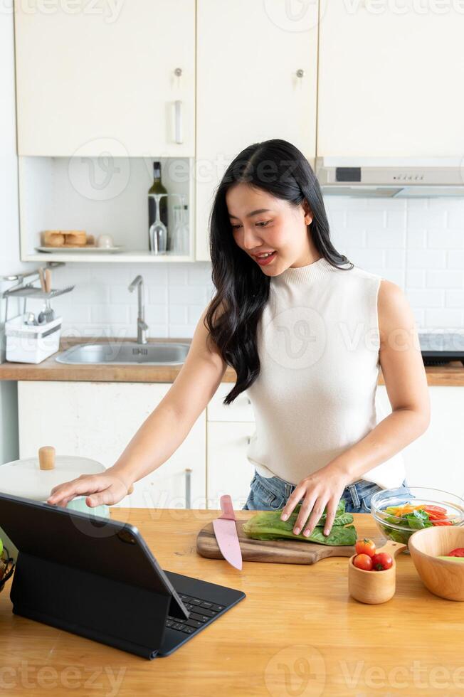 A gorgeous young Asian woman using her digital tablet while cooking in the kitchen. photo