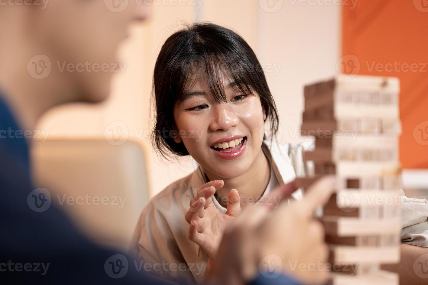 A young joyful Asian woman is enjoying playing a wooden block game with her friends, party at home. photo