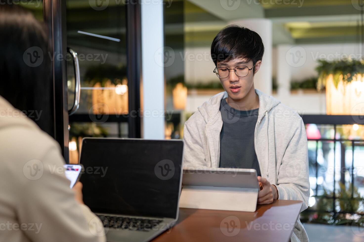 A young Asian male student is focusing on his work on his digital tablet in a cafe co-working space. photo