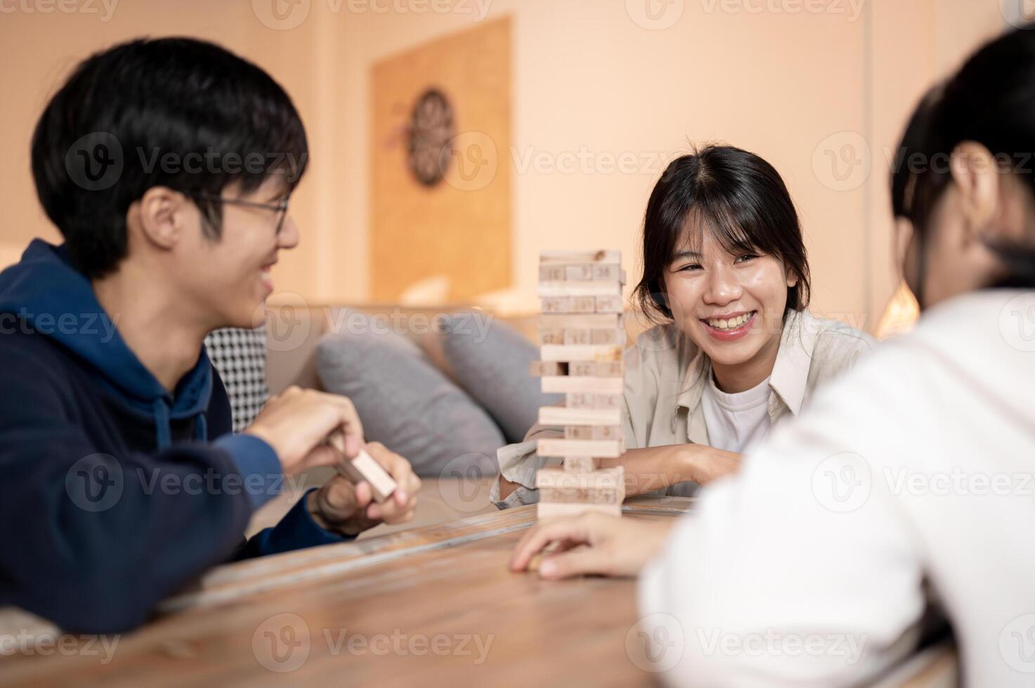 A happy Asian woman is playing wooden blocks at home, watching her friend remove a wooden block. photo