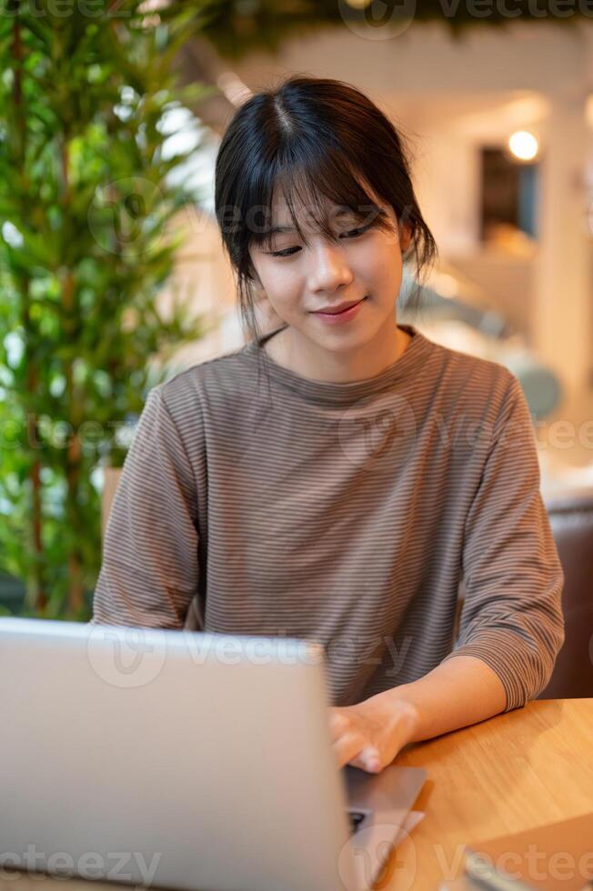 A young attractive Asian woman working remotely from a coffee shop, working on her laptop computer. photo