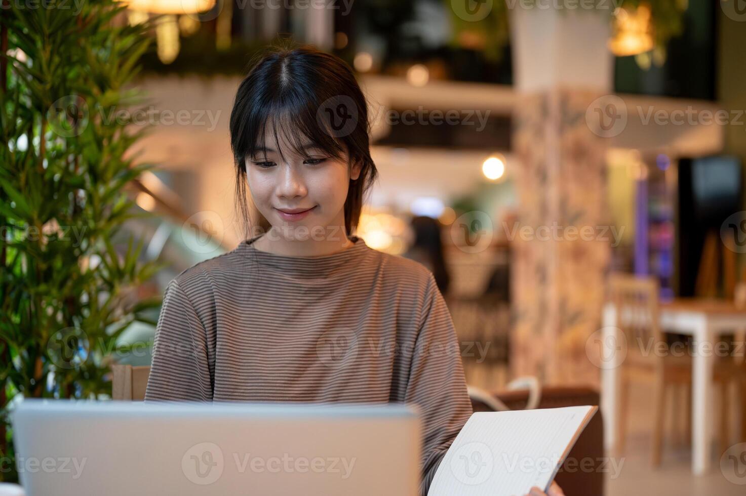 A woman working remotely from a cafe, working on her laptop and taking notes in her notebook. photo