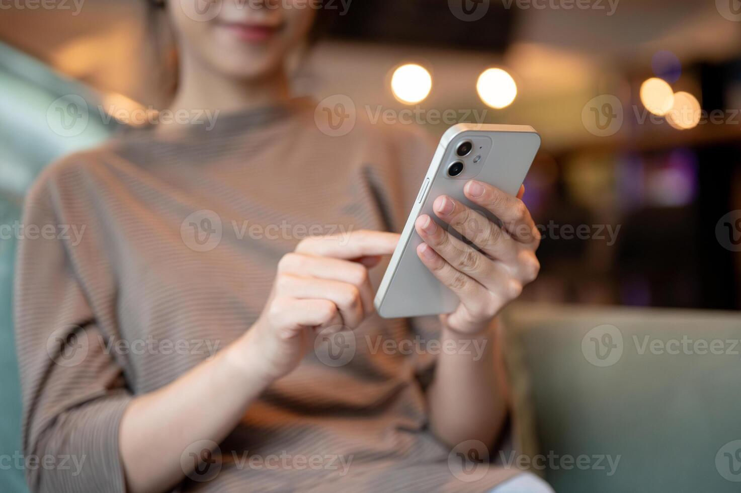 A cropped image of a woman using her smartphone while sitting at a sofa in a hotel lounge or a cafe. photo
