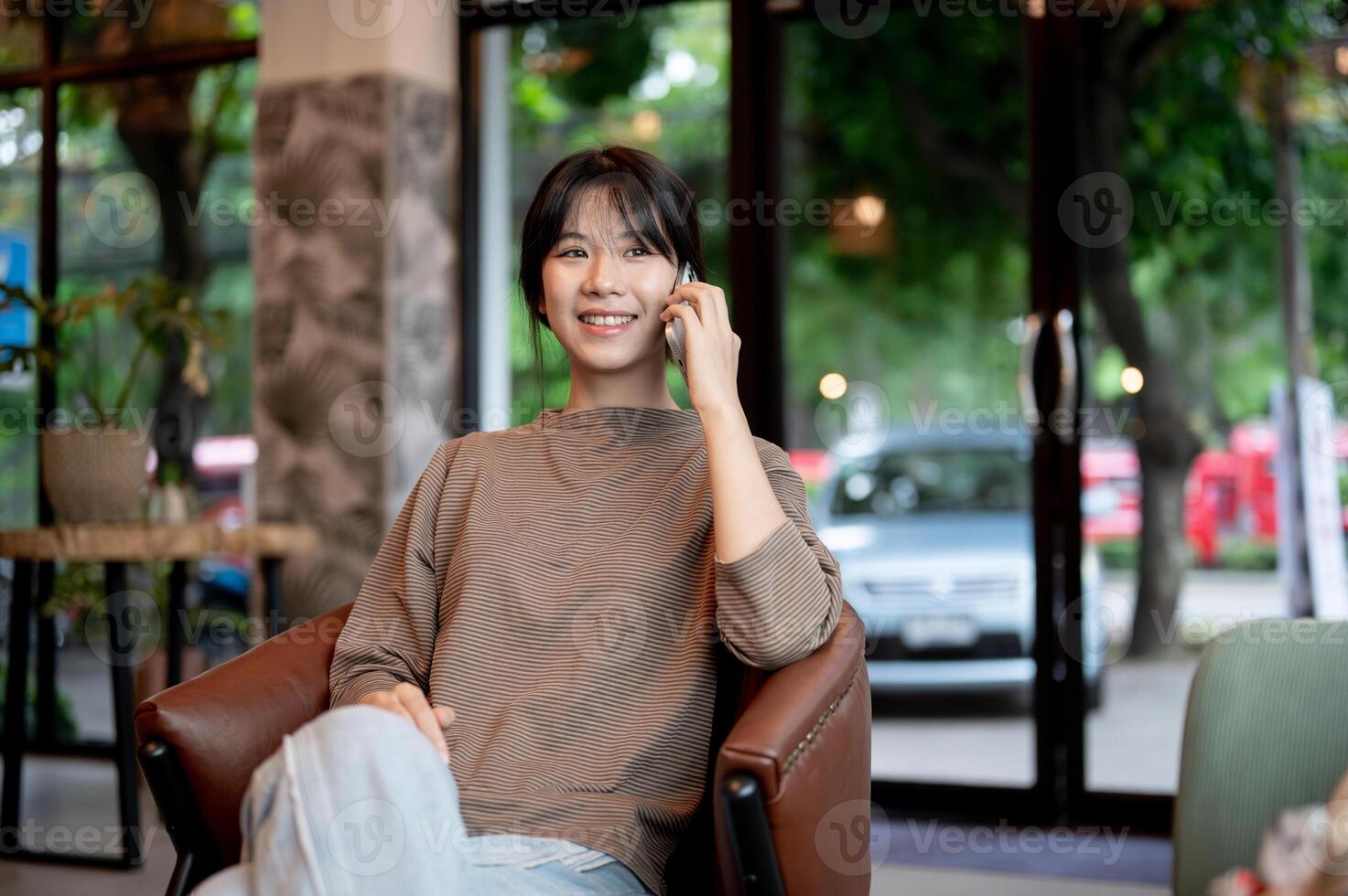 An attractive, positive Asian woman is talking on the phone with someone while sitting in a cafe. photo