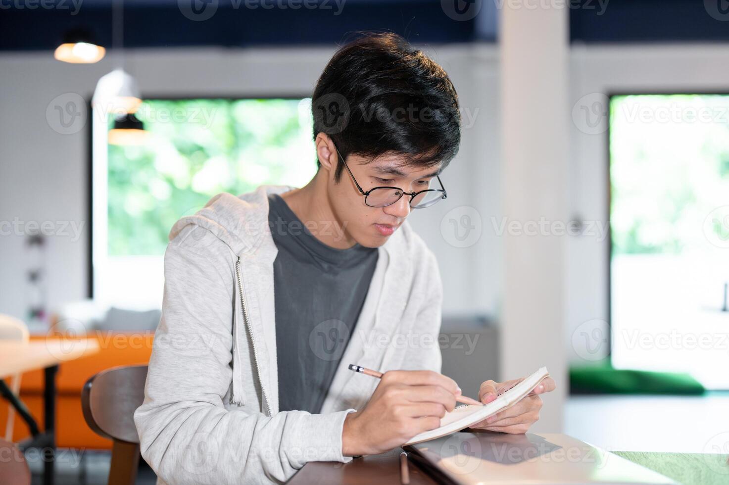 Smart Asian male college student is taking notes in his notebook or doing homework in a coffee shop. photo