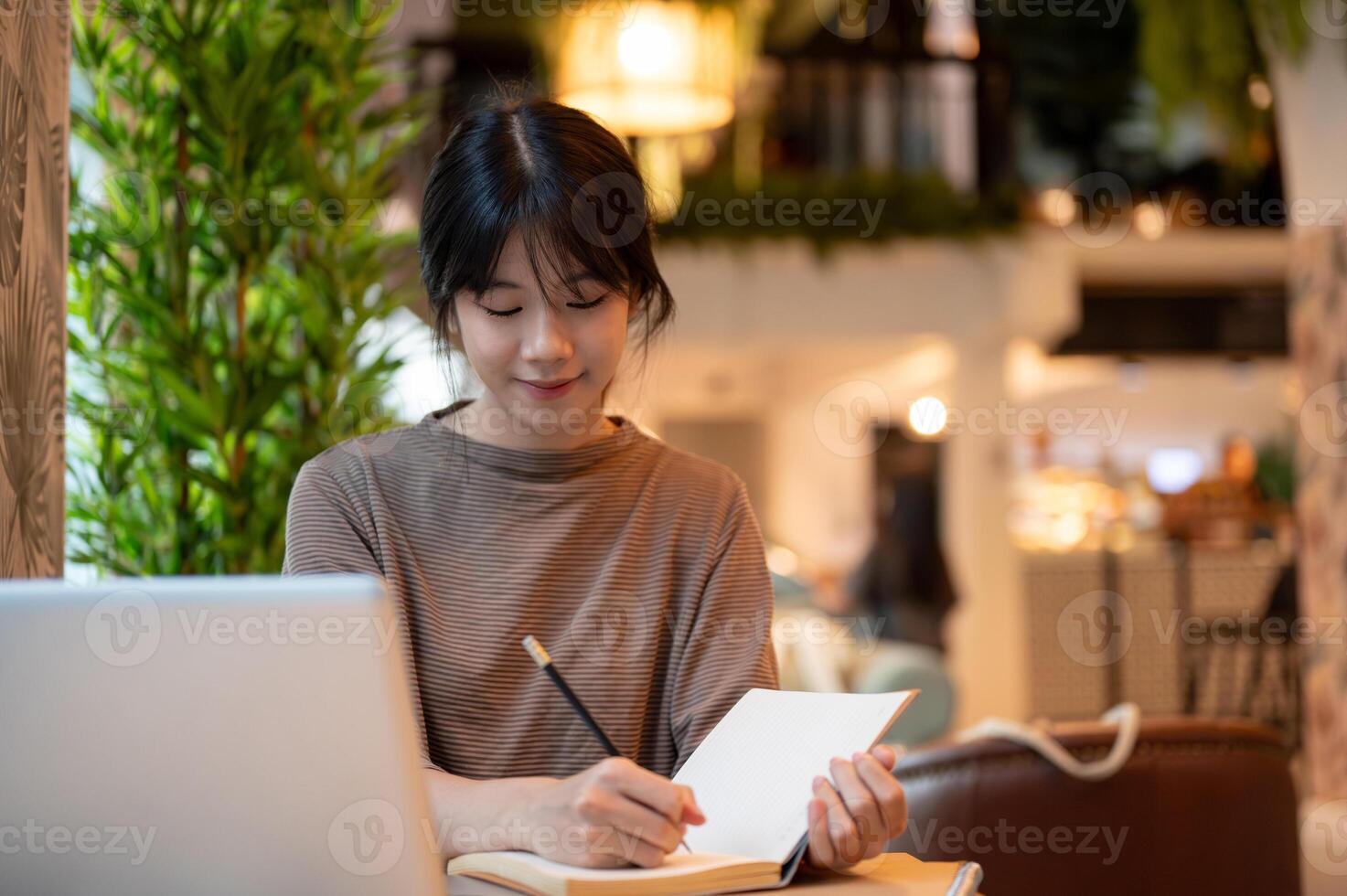 A woman working remotely from a cafe, working on her laptop and taking notes in her notebook. photo