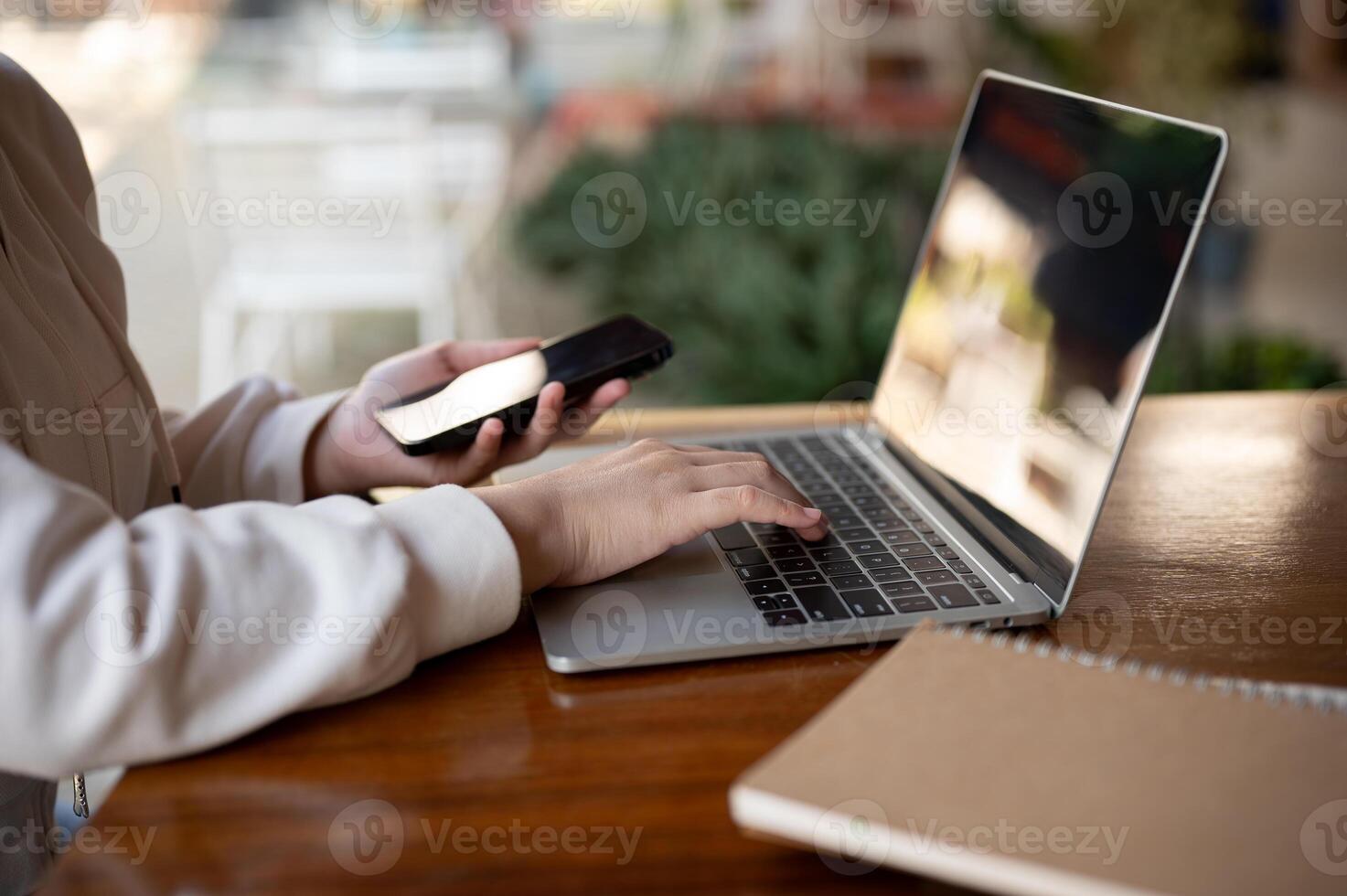 A woman in hoodie using her laptop computer at a table in a coffee shop, working remotely. photo