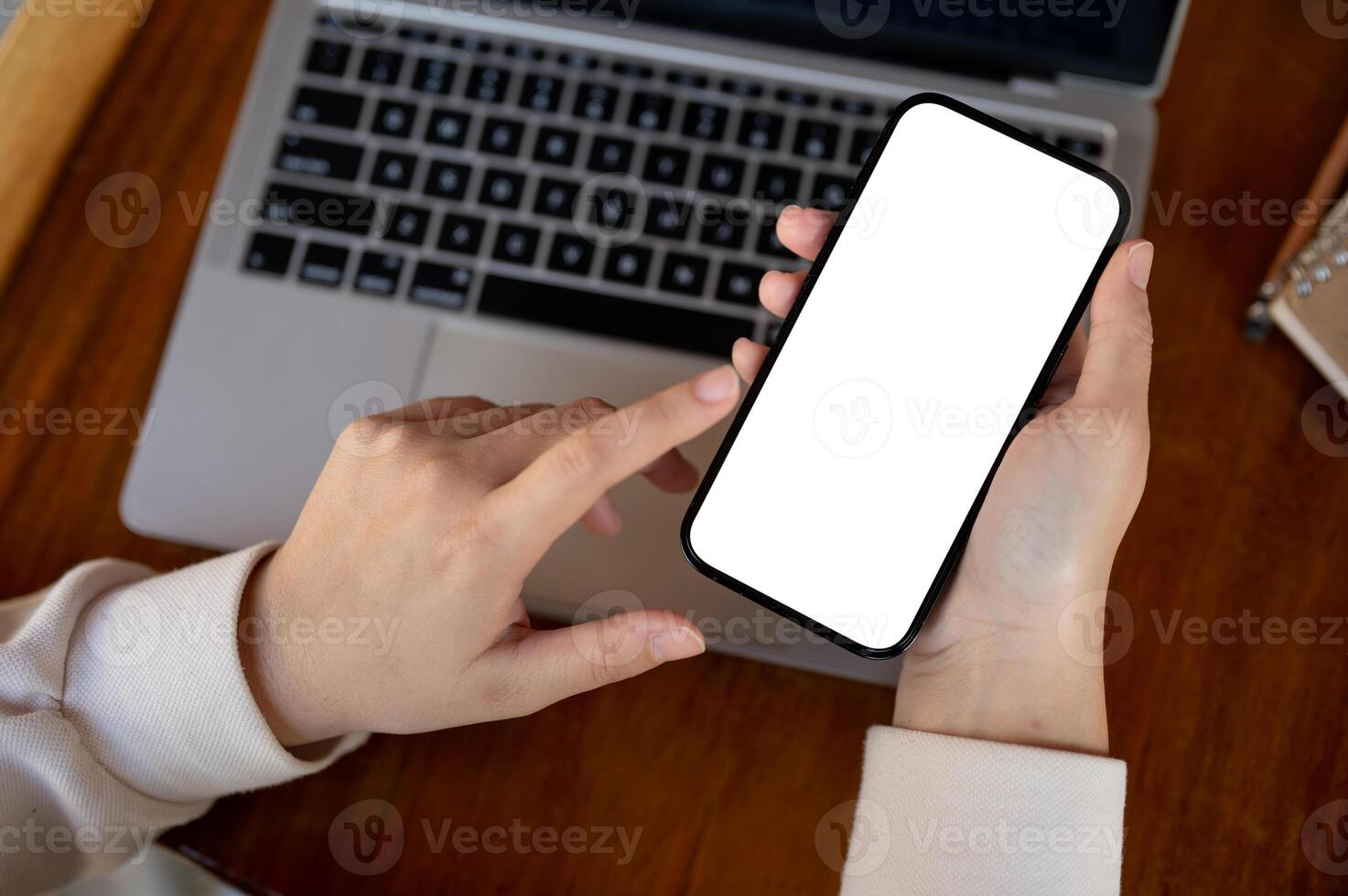 Top view image of a woman using her smartphone at her working desk. A white-screen smartphone mockup photo