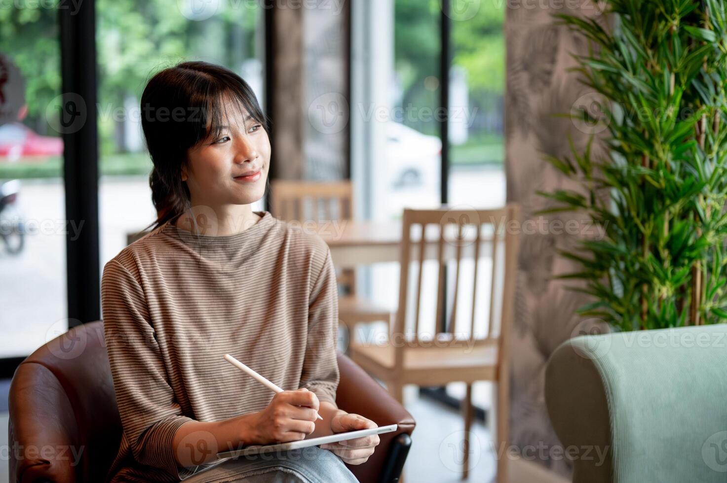 An attractive Asian woman with her tablet, gazing at the view outside of a cafe, daydreaming. photo