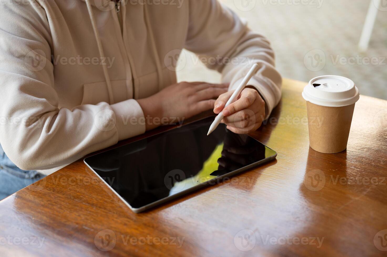 Cropped image of a woman in a hoodie is using her digital tablet at a table in a coffee shop. photo