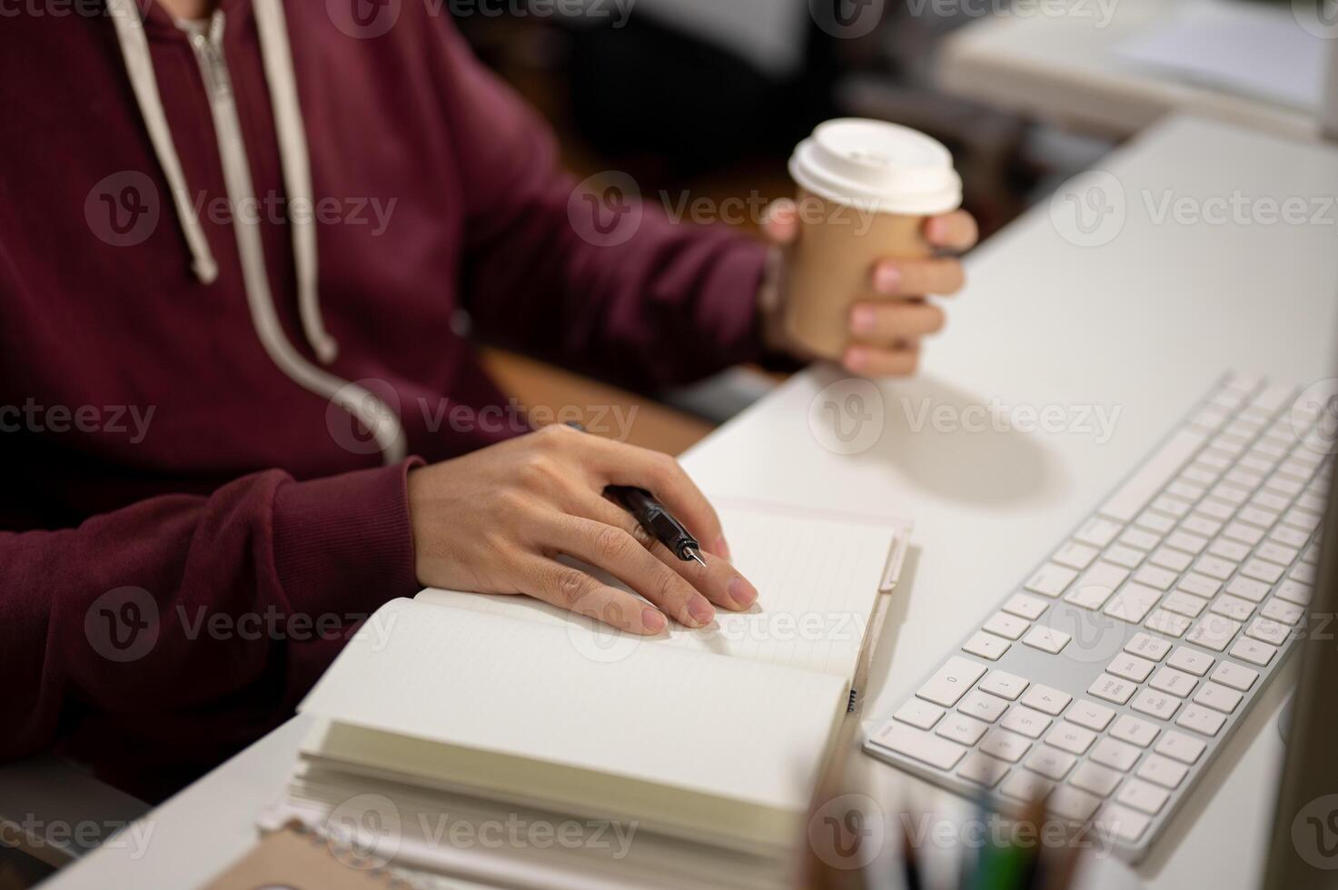 Cropped image of a man sitting in front of a computer, taking notes in a book, working in a room. photo