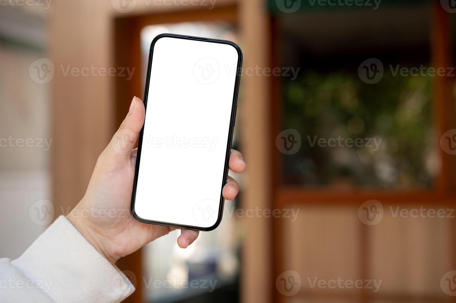 A woman's hand holding a white-screen smartphone mockup over a blurred background. photo