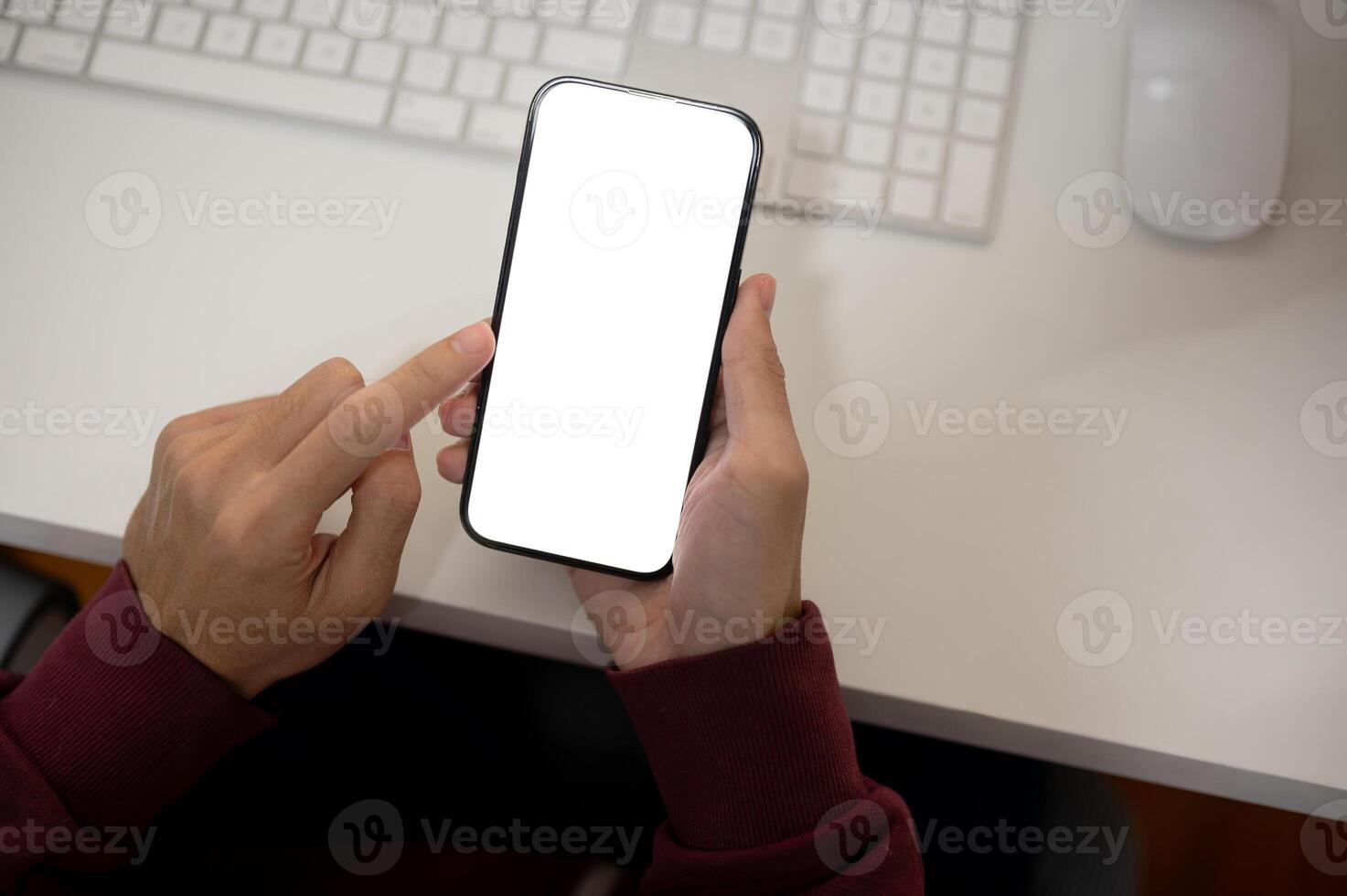 Top view image of a man using his smartphone at her office desk. A white-screen smartphone mockup photo