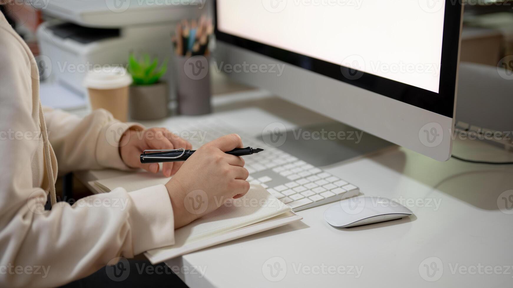 A woman is working on her tasks at her desk in the office, sitting in front of a computer. photo