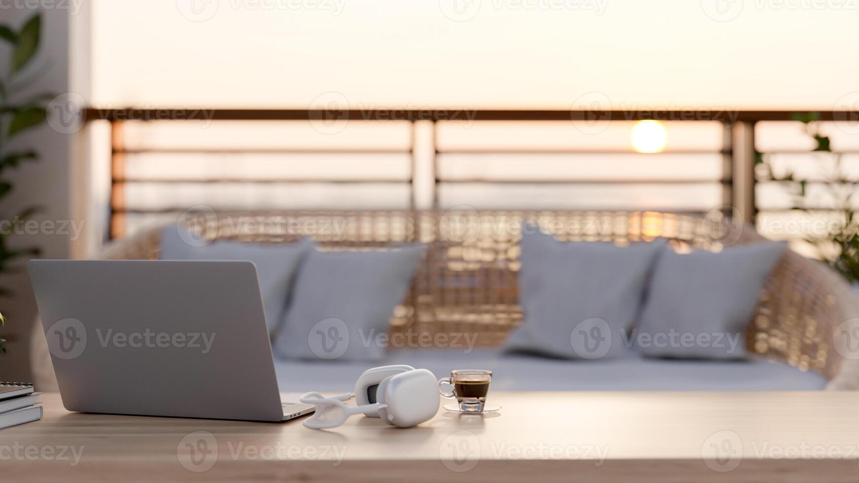 A computer, headphones, and a coffee cup on a wooden coffee table on a balcony with a wicker couch. photo