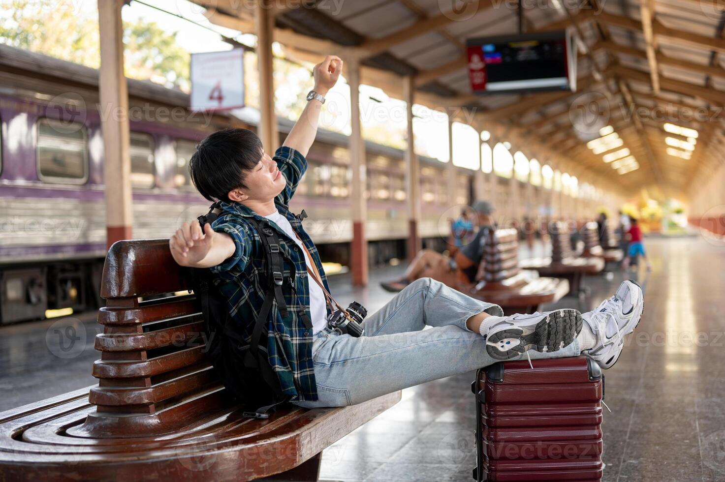 A carefree Asian man sitting on a bench, stretching his arms, relaxing while waiting for his train. photo