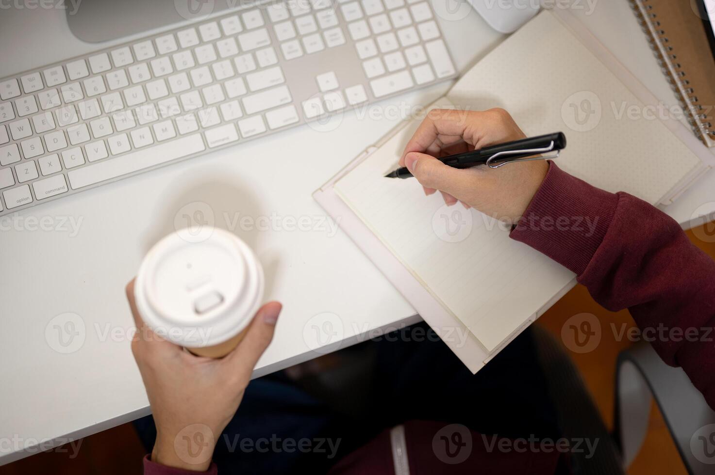Top view image of an office man taking notes in a book and sipping coffee at his office desk. photo