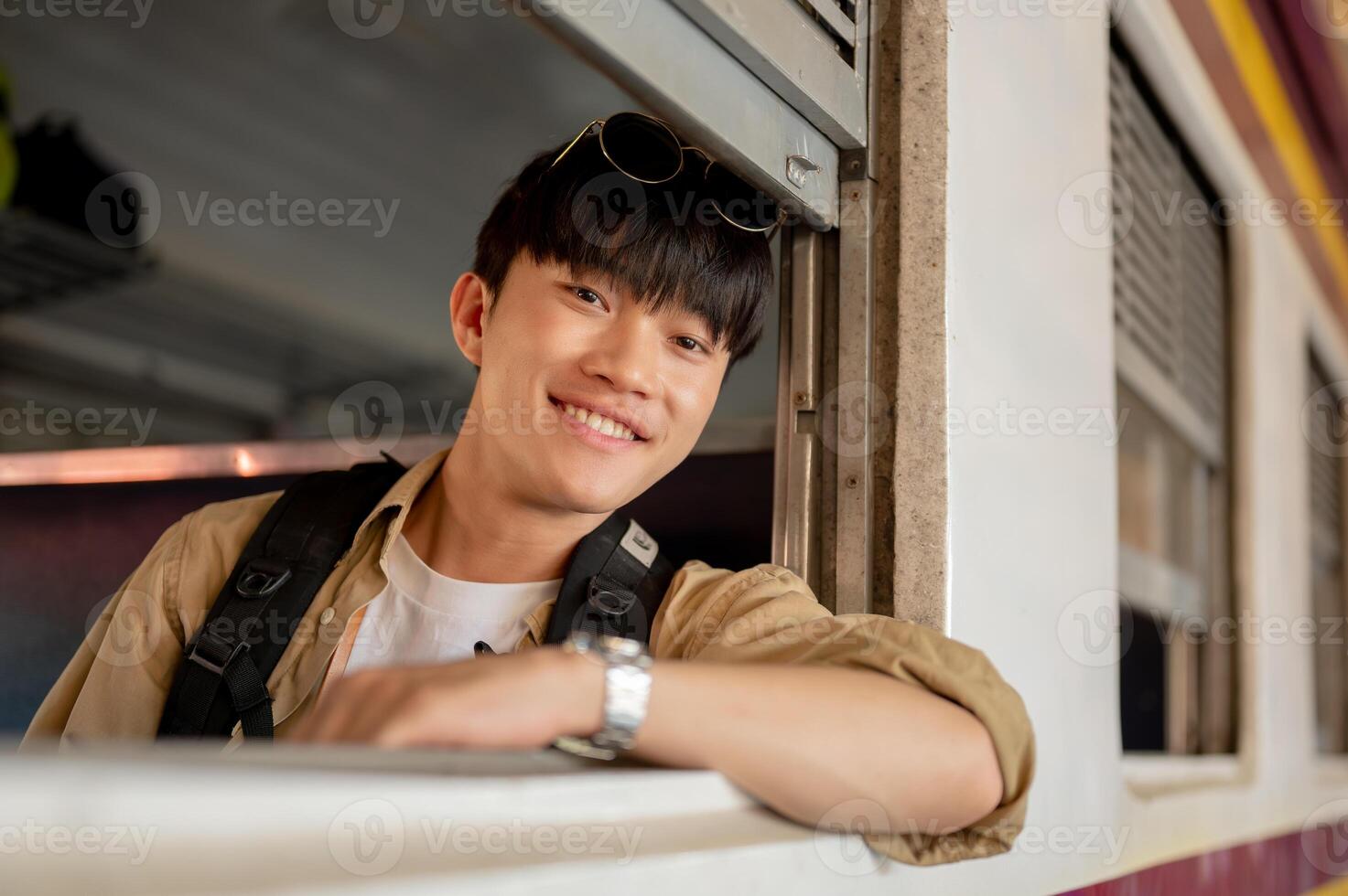 A happy young Asian man is on a train, sitting by the window and traveling somewhere by a train. photo