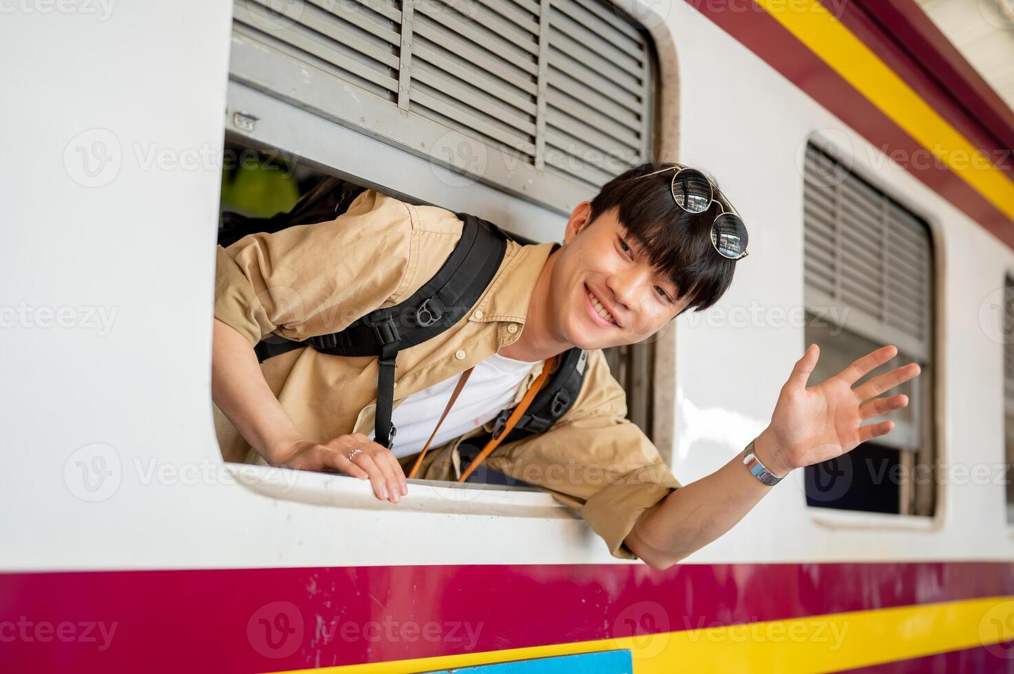 A happy Asian man is on a train, smiling and waving his hand, and traveling somewhere by a train. photo