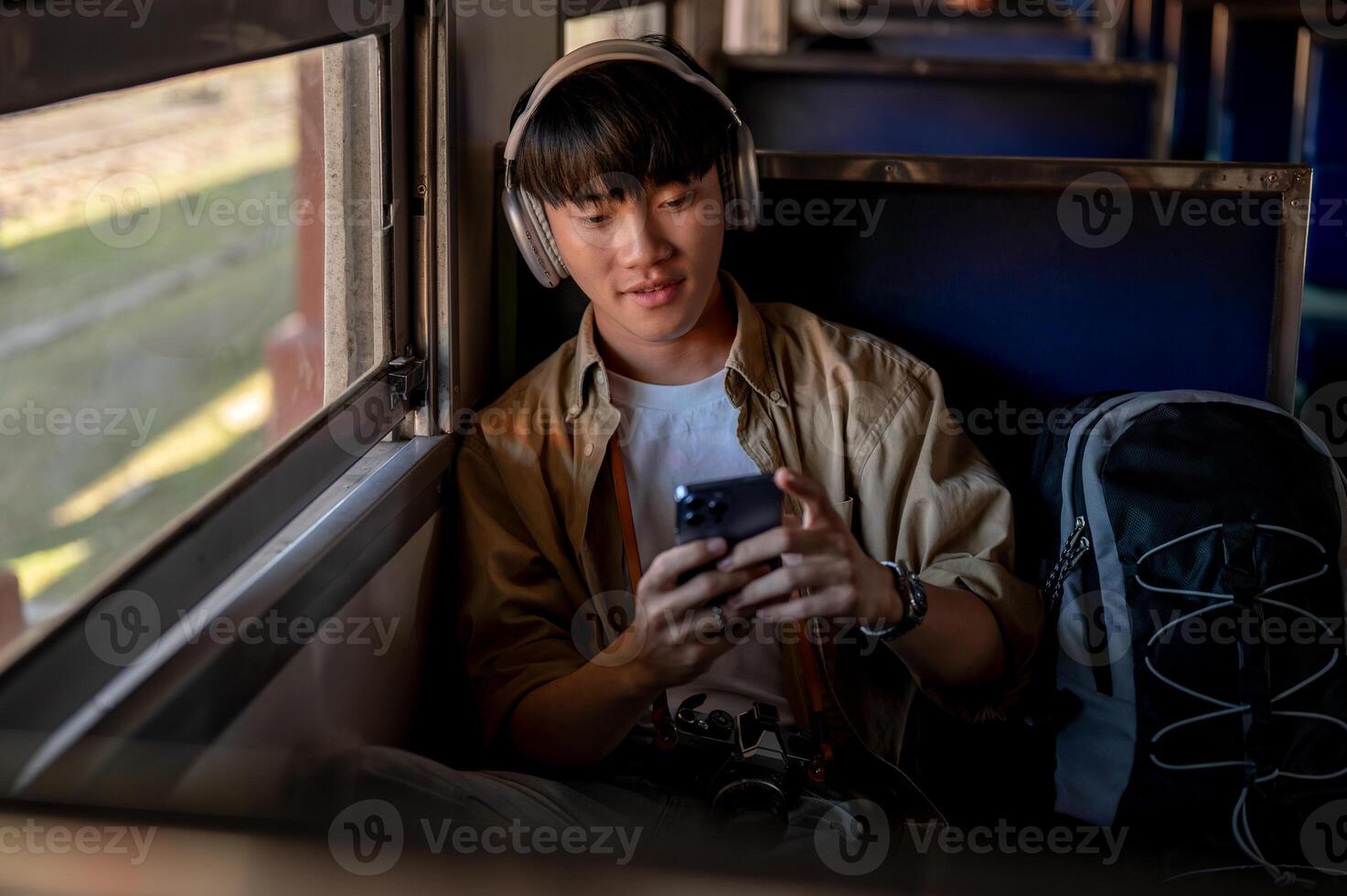 A happy Asian male is listening to music and using his phone while commuting by train to somewhere. photo