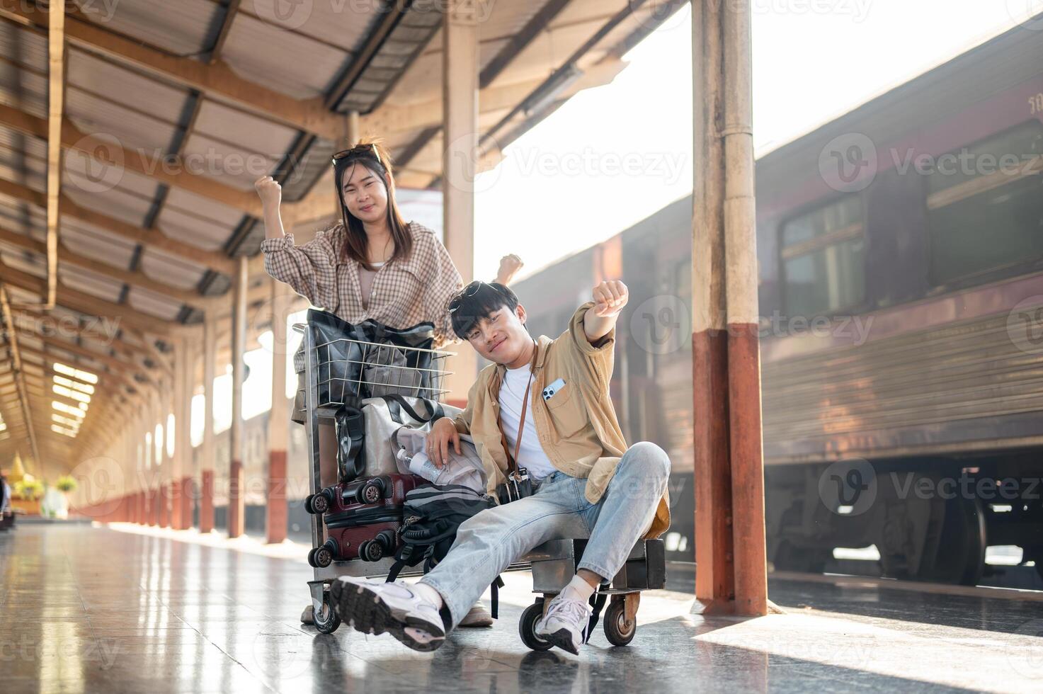 Cheerful couple are walking down the platform with a cart, commuting by a train at a railway station photo