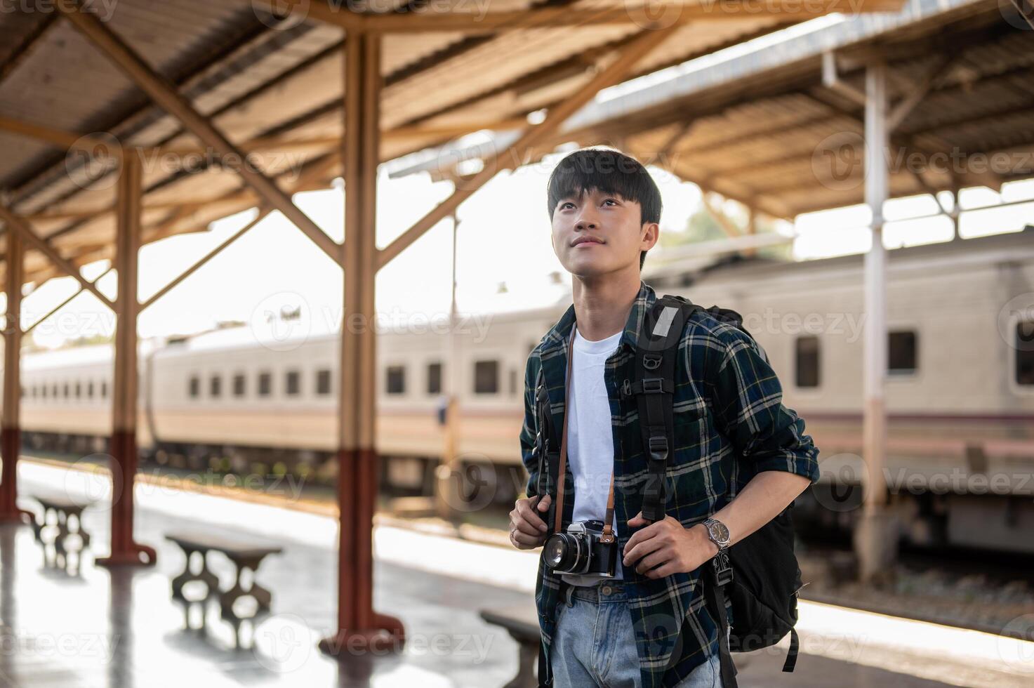A handsome, happy young Asian man tourist backpacker standing at a platform in a railway station. photo