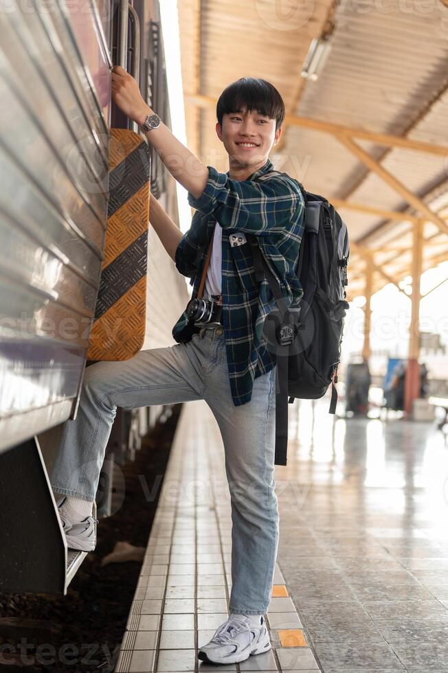A happy Asian man backpacker is getting on the train, travel somewhere on his summer vacation. photo