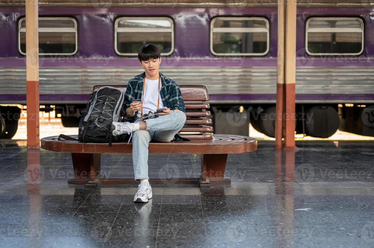 Handsome Asian man is paying his accommodation online on his smartphone while waiting for his train photo