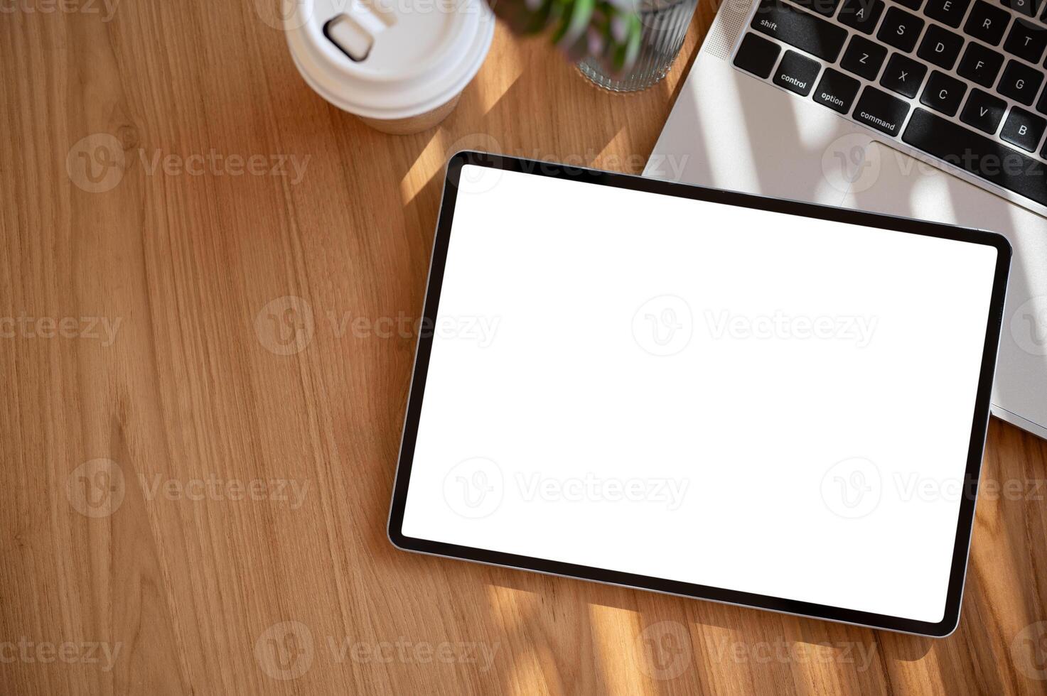 A wooden desk with a digital tablet mockup, a tablet pen, a coffee cup, and a laptop computer. photo