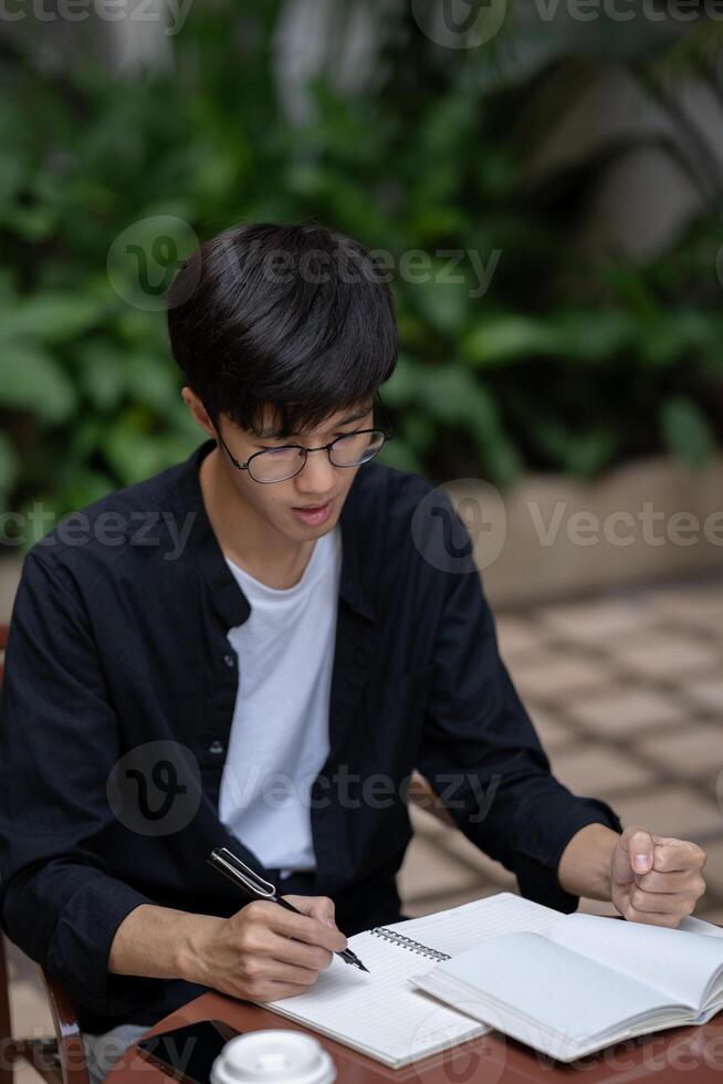 A dissatisfied and unhappy Asian man is working on his tasks at a table outdoors. photo