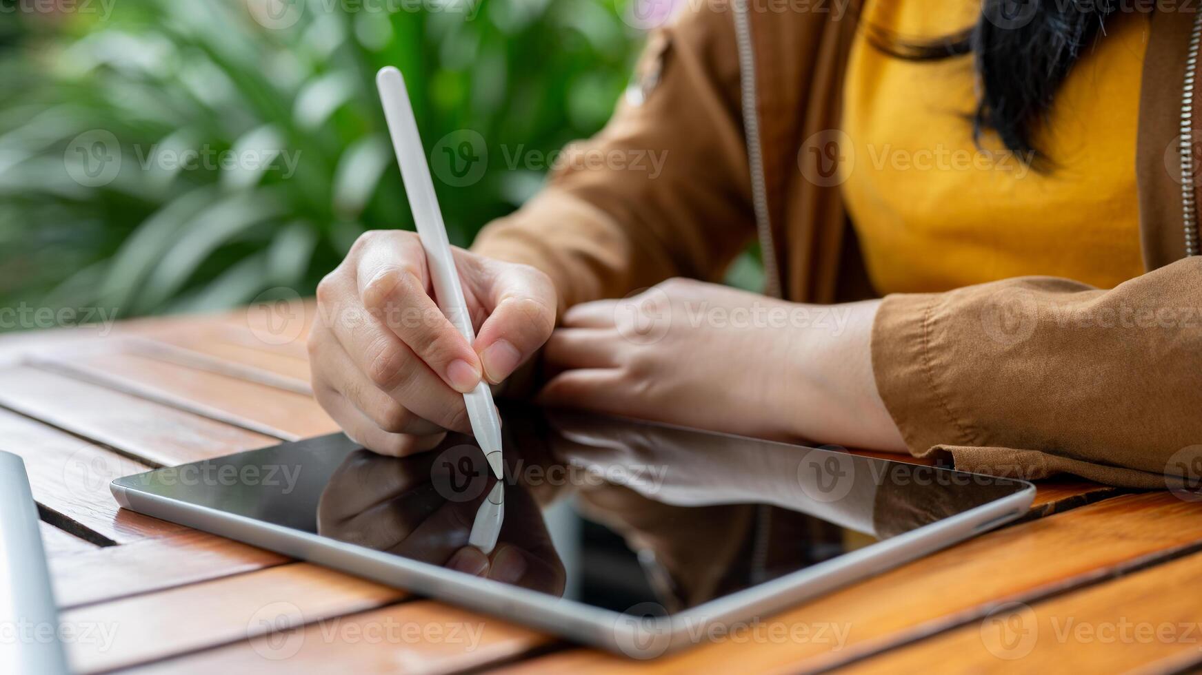 A cropped image of an Asian woman sits at an outdoor table and uses her digital tablet. photo
