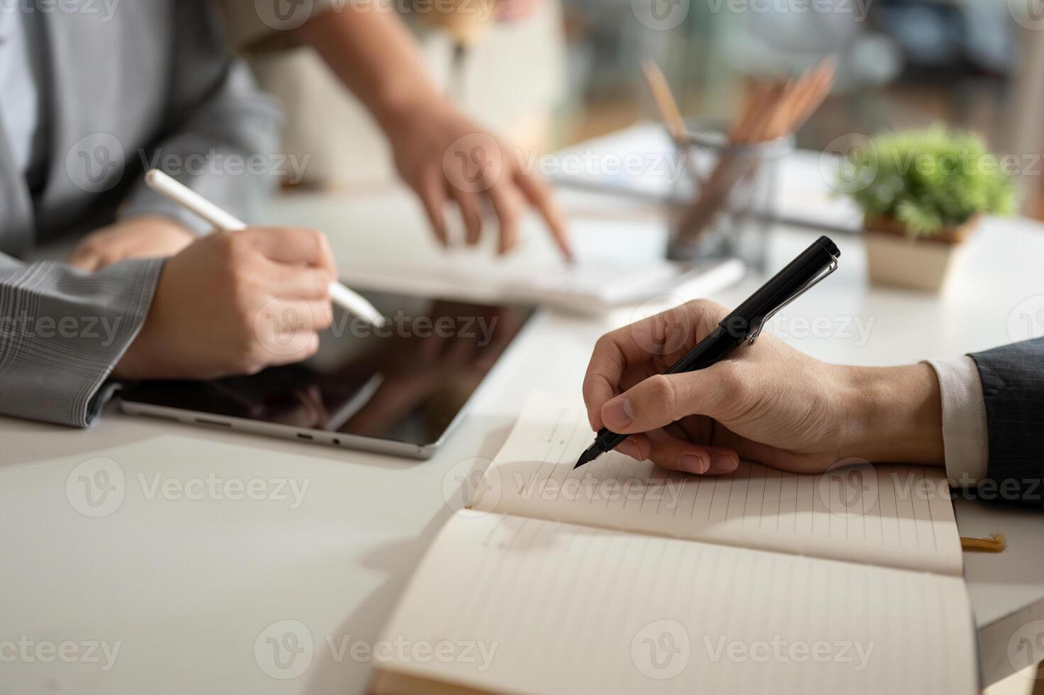 A businessman is taking notes on a notebook while having a meeting with his team in the office. photo