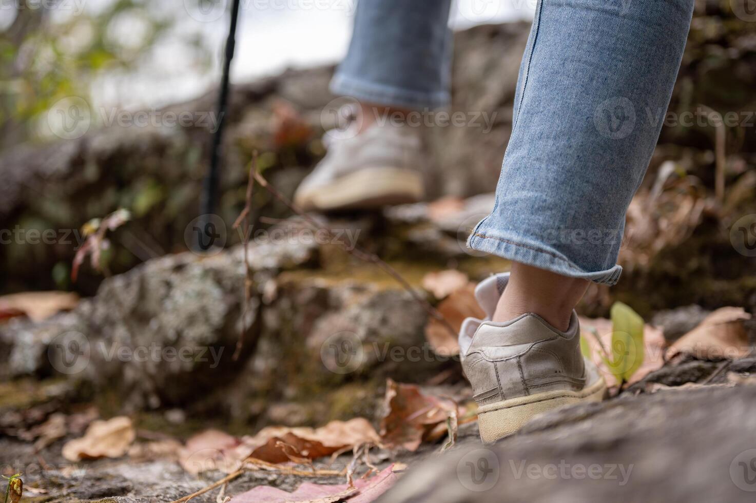 Close-up legs image of a woman is hiking with a trekking pole on the rock mountain. photo