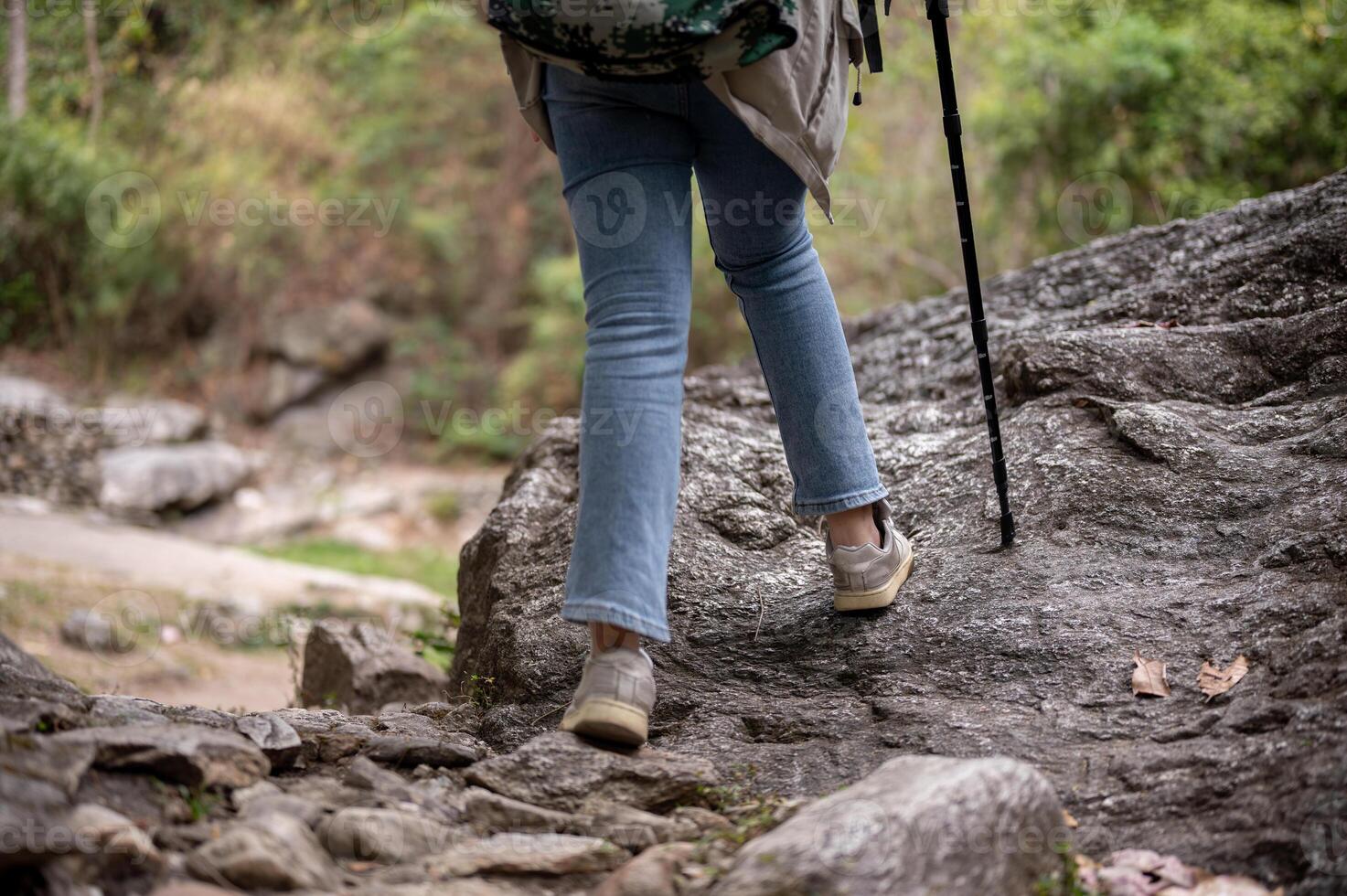 Close-up legs image of a woman is hiking with a trekking pole on the rock mountain. photo