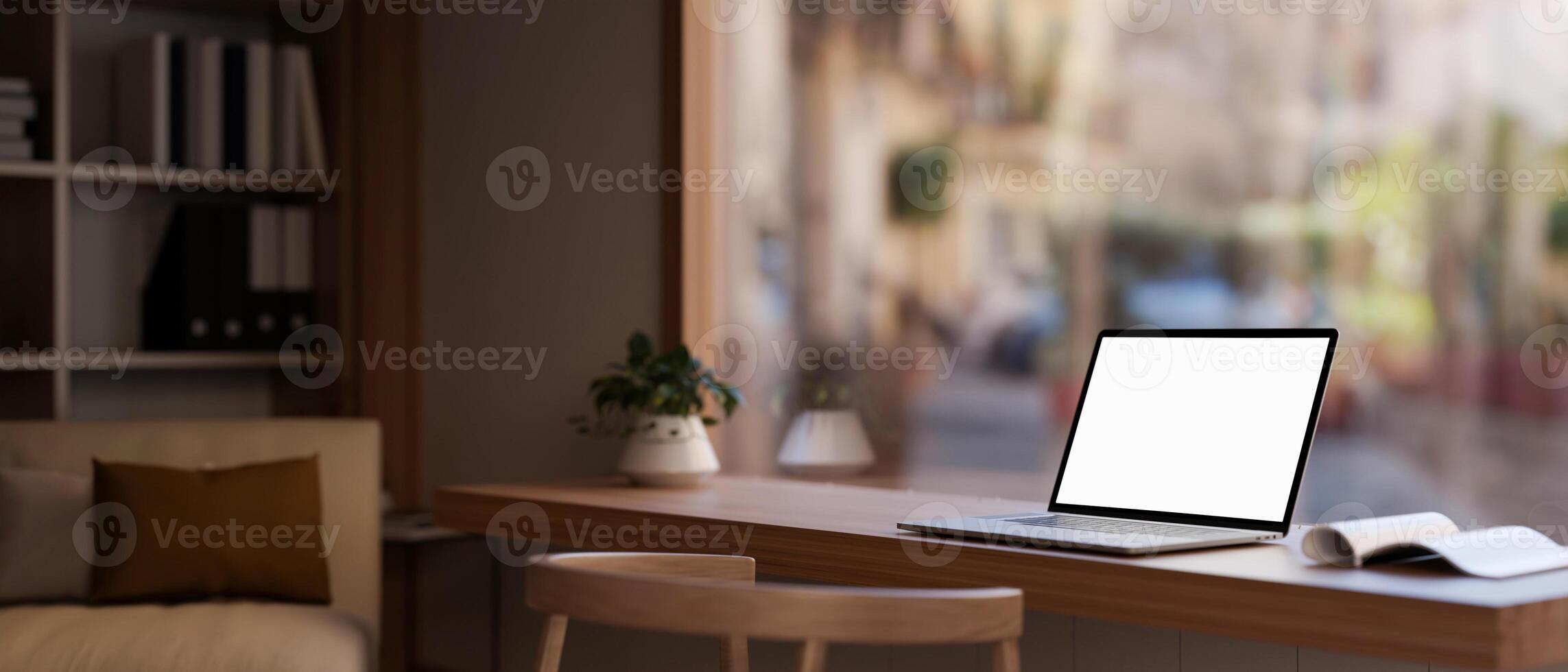 A white-screen laptop computer on a table near a large glass window in a modern cosy room. photo