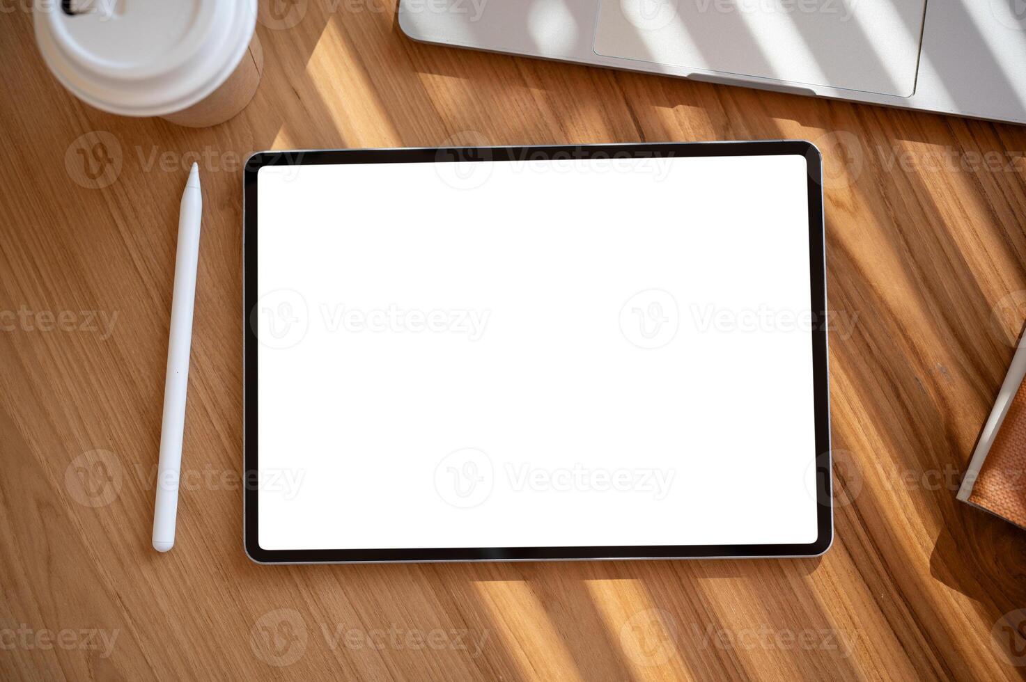 A wooden desk with a digital tablet mockup, a tablet pen, a coffee cup, and a laptop computer. photo